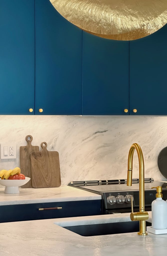 MandiCasa Yota cabinets in a deep blue hue with round handles in bronze finish. White Quartzite countertops and backsplash with grey veins.