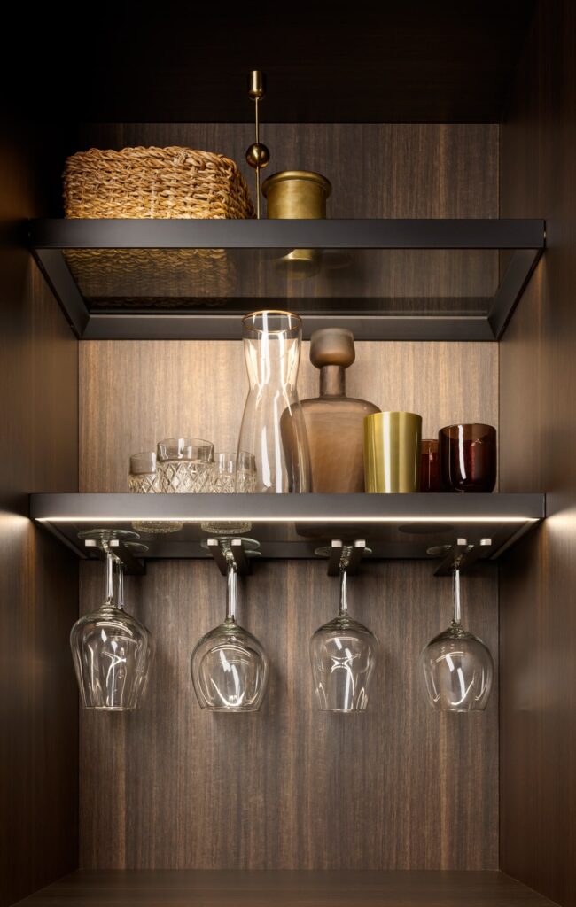 Bespoke kitchen cabinet interior with LED-lit glass shelves fitted with custom stemware holders.